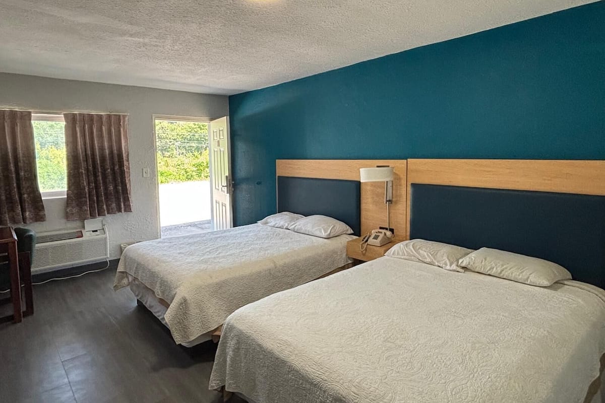 A hotel room with two beds, a desk, and a window with curtains.