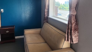 Una habitación con un sofá color beige, una ventana con cortinas, una mesita de noche de madera oscura y una pared azul.