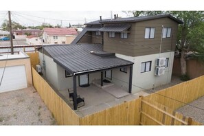 A residential building with a covered patio area, air conditioning units, and a fenced yard.