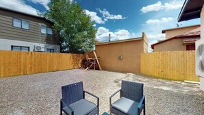 Un patio trasero con dos sillas de mimbre, una cerca de madera y un edificio al fondo.