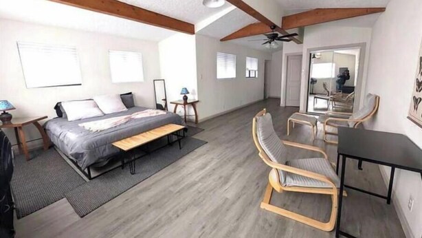 Un dormitorio con cama, mesitas de noche, escritorio y una silla. Cuenta con un ventilador de techo y una ventana con persianas.
