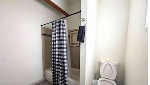 Un baño con cortina de ducha, inodoro y un pequeño cubo de basura.