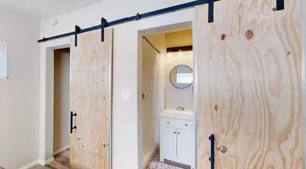 Un couloir avec une porte coulissante en bois, un meuble blanc et un miroir au mur.