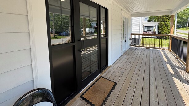 A covered porch with a wooden deck, a black door, and a view of the street. - Cozy 2-Bed Apartment in Town (Wolfville)