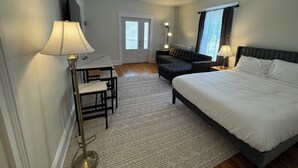 A hotel room with a bed, a desk with a chair, a sofa, a standing lamp, and a patterned rug. - Cozy 2-Bed Apartment in Town (Wolfville)