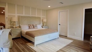 A bedroom with a large bed, two bedside tables with lamps, a wooden floor, and a white door.