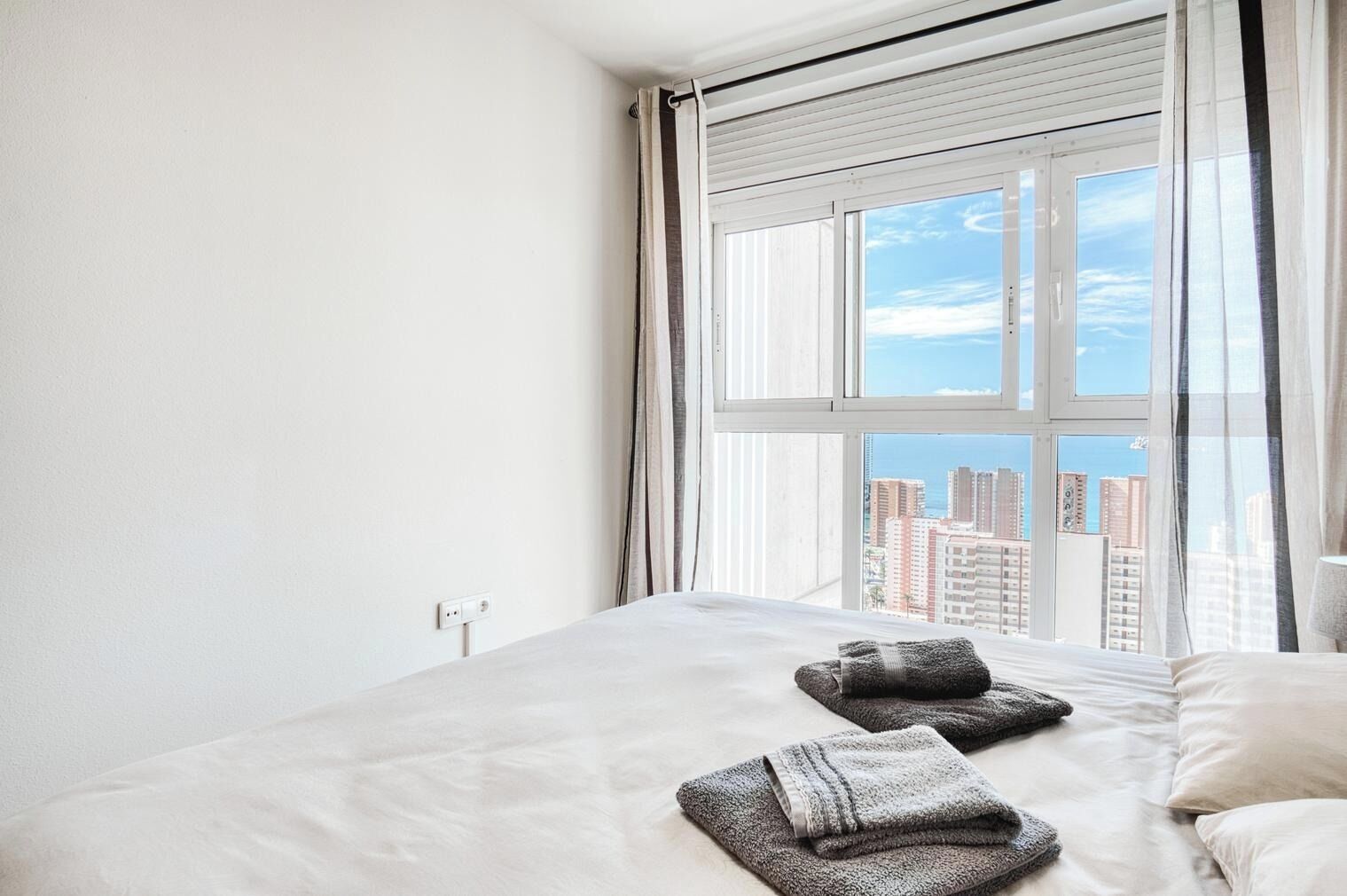 Habitación de hotel con una cama grande, una ventana con persianas y vistas a la ciudad.