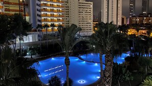A nighttime view of a hotel with a pool area surrounded by palm trees and modern buildings. - Siroco-Gemelos 22 (Benidorm)