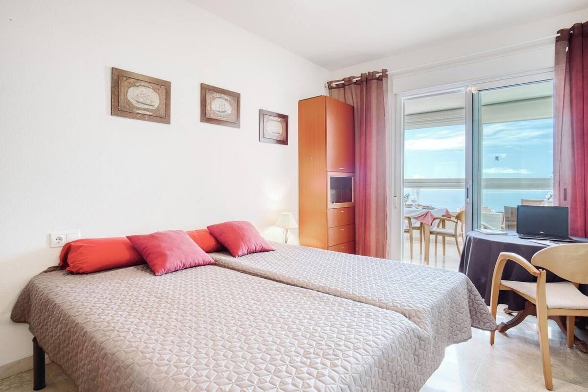 Ein Hotelzimmer mit Bett, Schreibtisch mit Laptop, Stuhl und Meerblick durch ein großes Fenster.