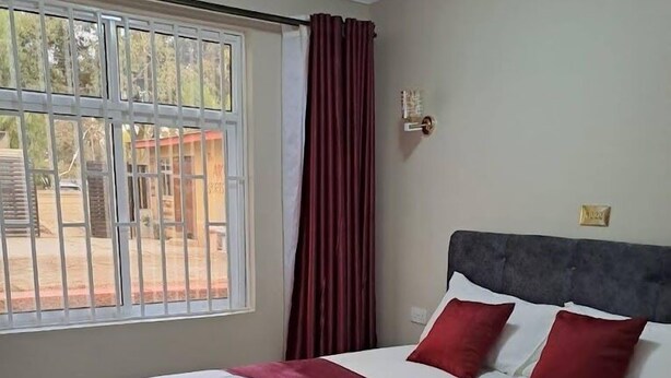 A neatly made bed with white and red bedding, a grey headboard, and a window with curtains.
