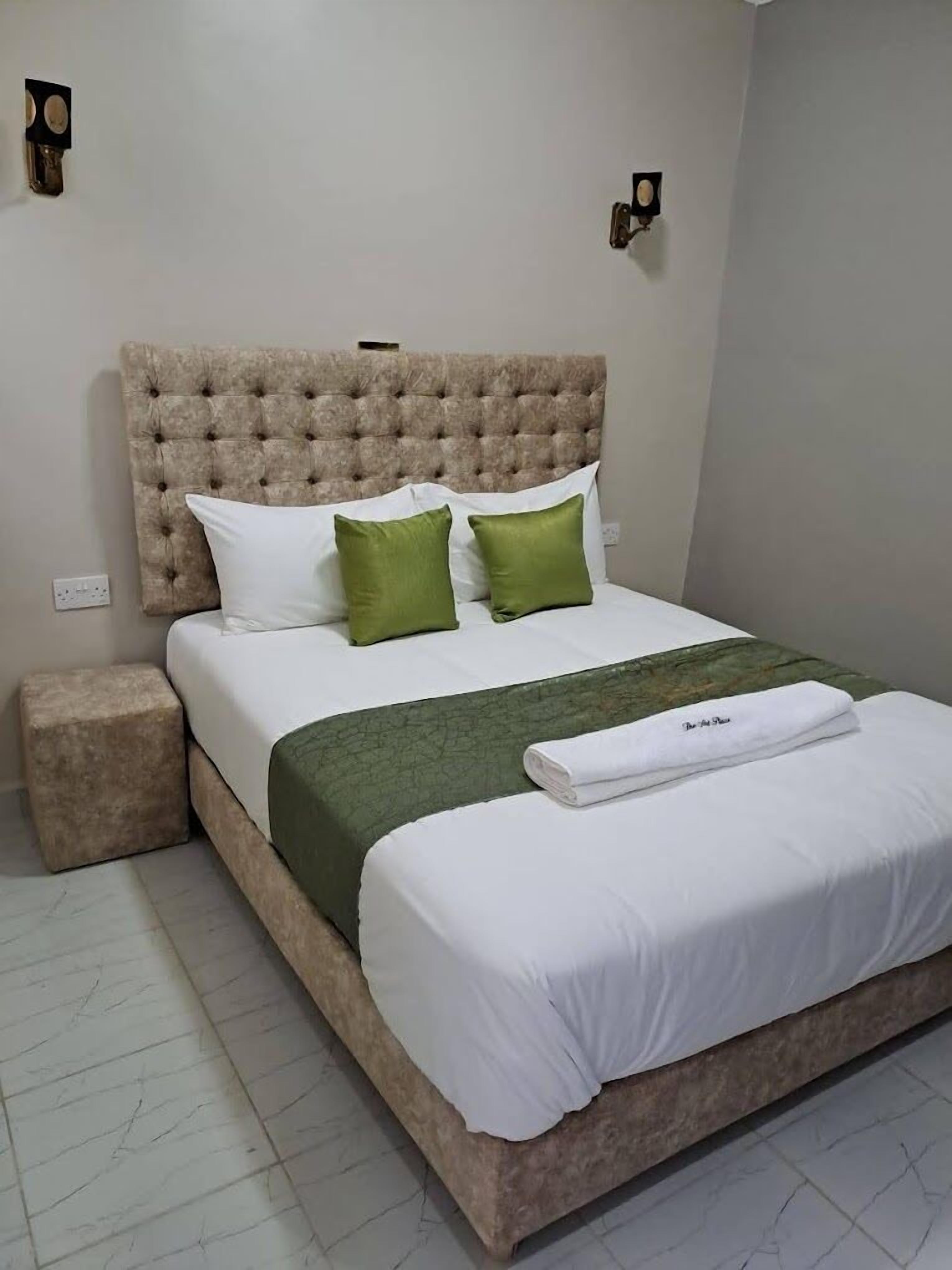 A bed with a tufted headboard, white and green pillows, a green bedspread, and a white towel on the footboard.