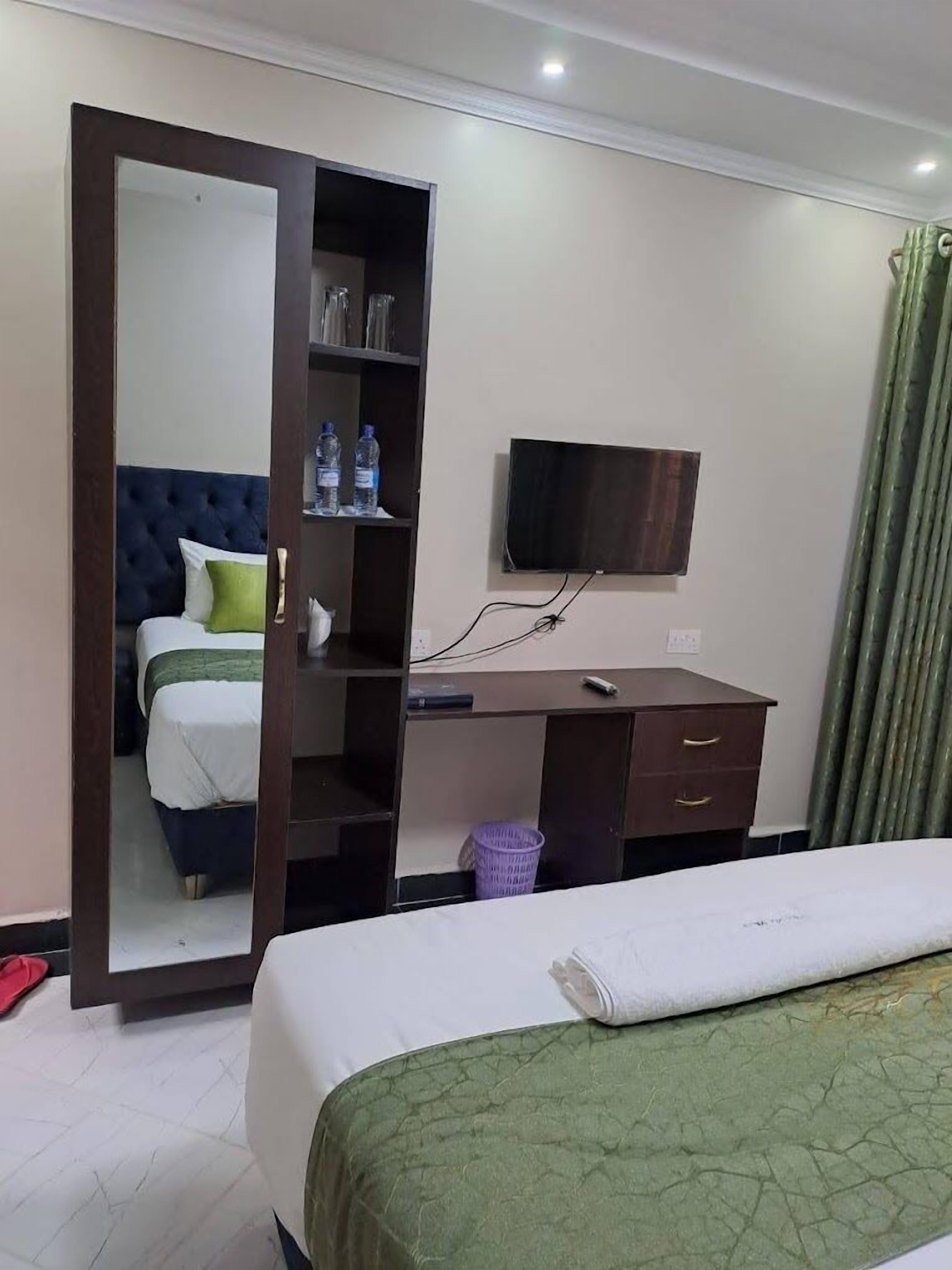 A hotel room with a bed, a desk with a chair, a television, and a wardrobe.