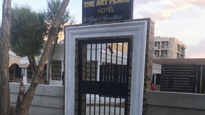 The Art Place Hotel with a gated entrance, a signboard, and a paved pathway leading to the gate.