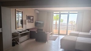 A spacious living room with a large window, a flat-screen TV, a sofa, a coffee table, and a dining area with a table and chairs.