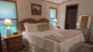 Un letto rifatto con un piumone bianco, un cuscino decorativo e un asciugamano piegato su un tappeto fantasia.