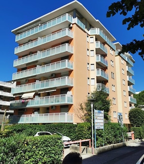 A multi-story residential building with balconies, a parking area, and a signboard. - Inviting Apartment With Lateral sea View (San Michele al Tagliamento)