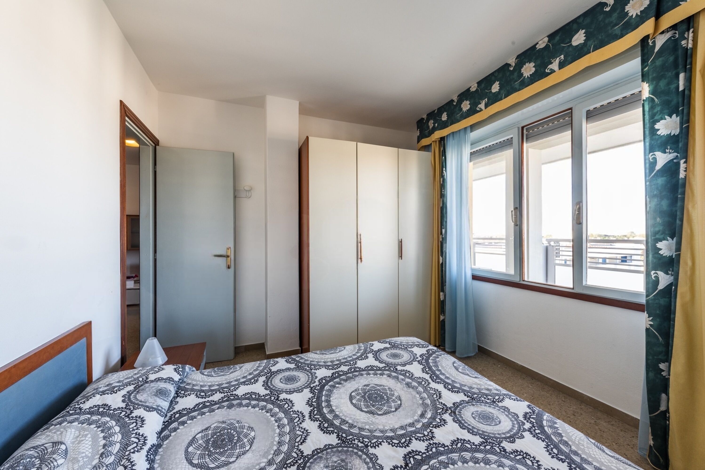 A bedroom with a bed, a wardrobe, and a window with curtains.
