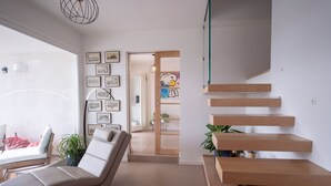 A modern living room with a lounge chair, a staircase with wooden steps, and a wall decorated with framed pictures.
