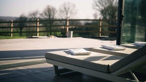 Un espace de détente extérieur moderne, doté de sièges rembourrés et d’une paroi en verre.