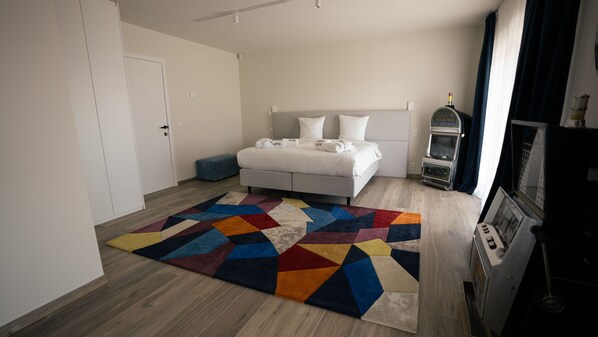 A bedroom with a bed, a colorful geometric rug, a minibar, and a window with curtains.