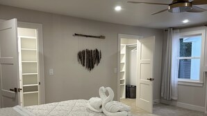 Een slaapkamer met een groot bed, een plafondventilator, een kledingkast en een raam met gordijnen.