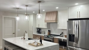 Een moderne keuken met een groot kookeiland, roestvrijstalen apparatuur en hanglampen.