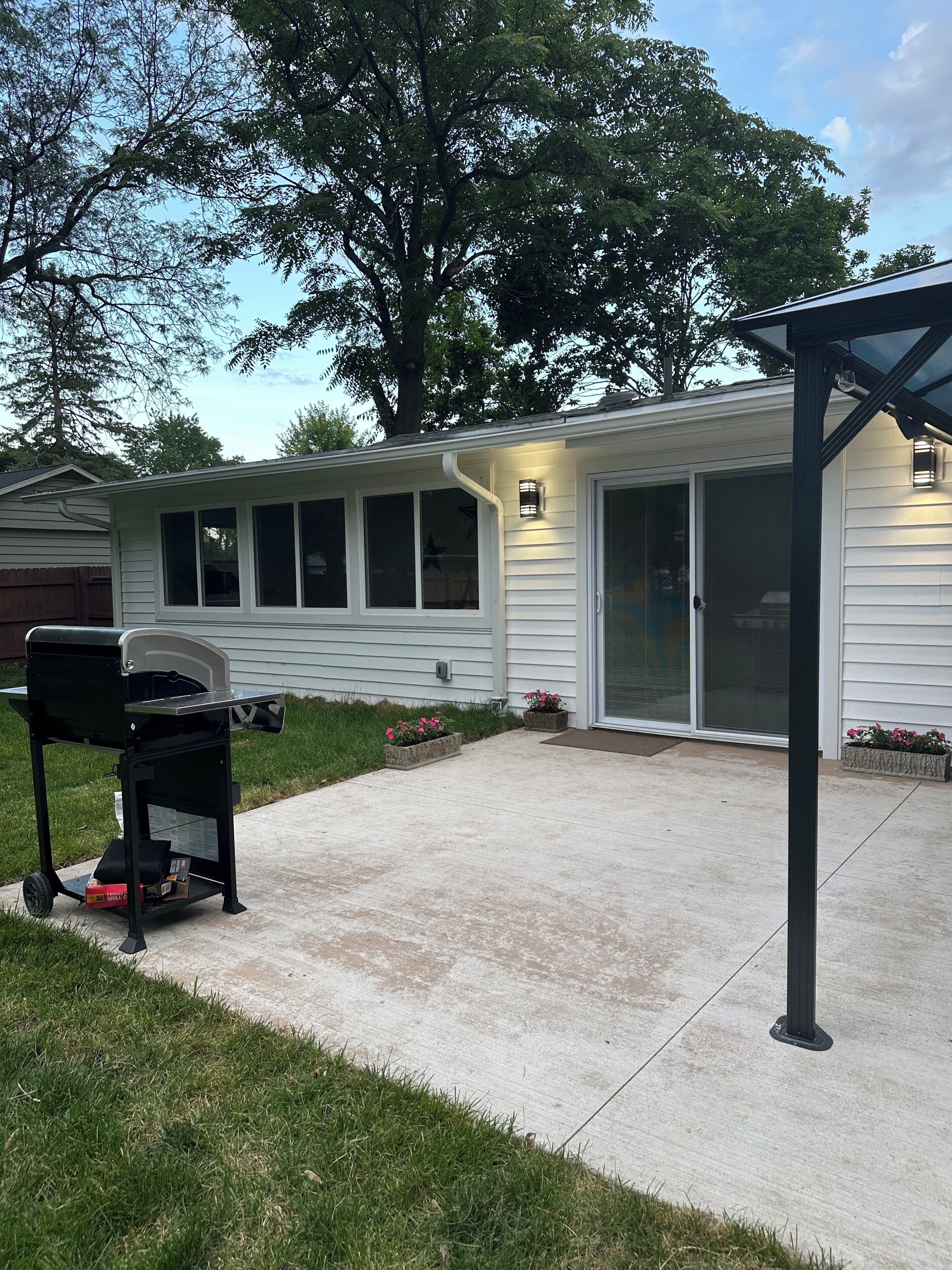 A backyard with a barbecue grill, a covered patio, and a sliding glass door.