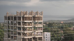 Un immeuble en construction, composé de plusieurs étages, avec des échafaudages apparents et une vue sur le paysage urbain en arrière-plan.