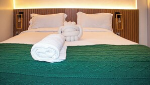 Un lit bien fait, avec une couverture verte, des oreillers blancs et une serviette enroulée.