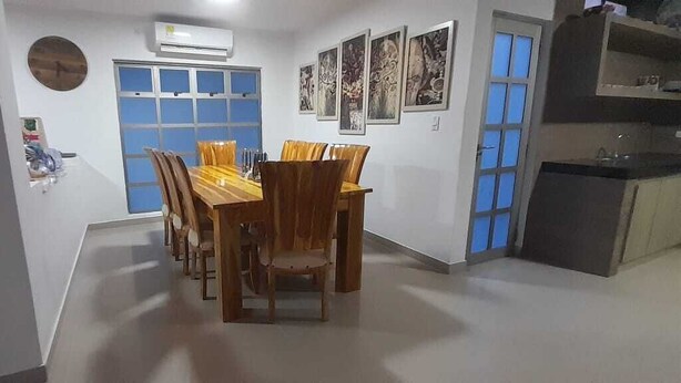 Un comedor con mesa y sillas de madera, una ventana con vidrio azulado y una zona de cocina con armarios y encimera.