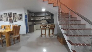 A dining area with a wooden table and chairs, a kitchen in the background, and a staircase. - Cabaña de Enseño en Coveñas (Coveñas)