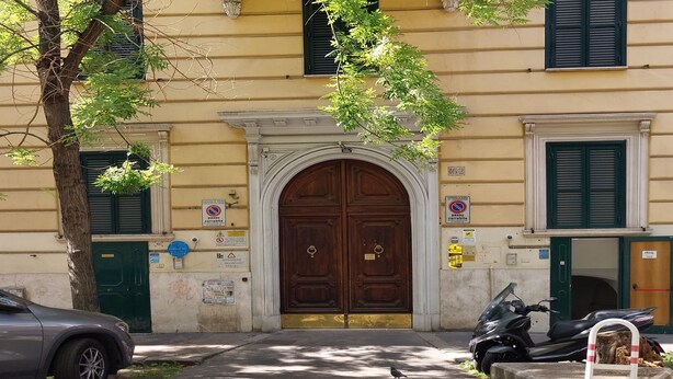 Un edificio con un gran portal de madera doble, un árbol en primer plano y una moto estacionada.