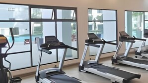 Een sportschool met loopbanden en fitnessapparatuur, grote ramen en uitzicht op een zwembad.