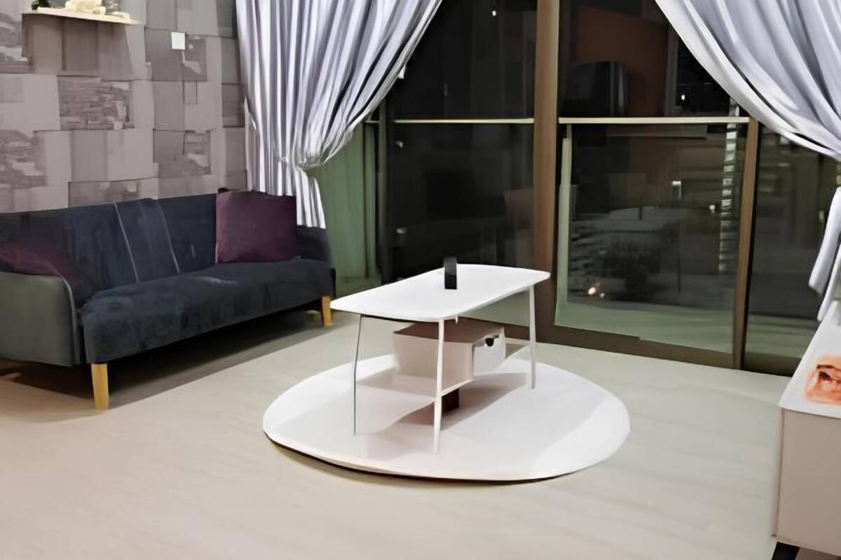 A modern living room with a round white table, a grey sofa, and a glass door leading to an outdoor area.