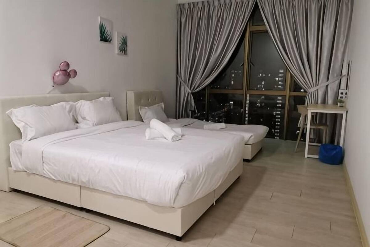 A hotel room with a large bed, a smaller bed, a desk, and a view of the city through the window.