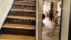 Una escalera de madera que conduce a una habitación con una pared de piedra y piso de baldosas.