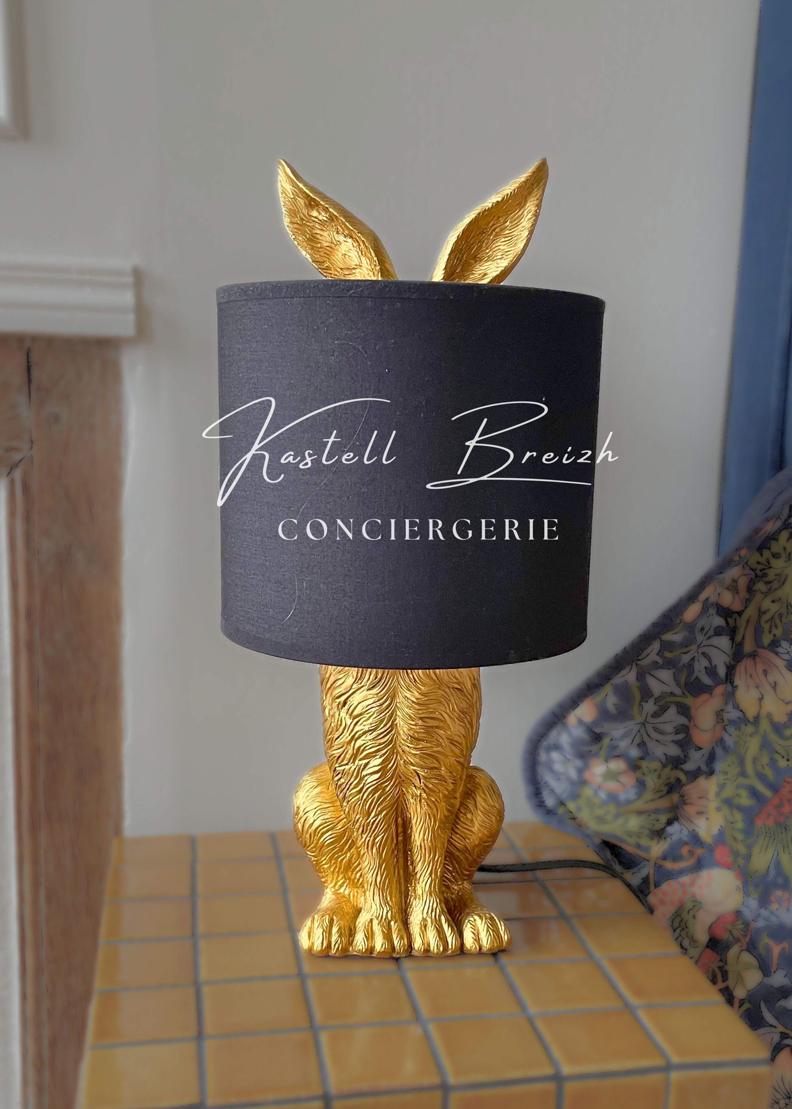 Een decoratieve lamp met een zwarte voet en een gouden konijnenbeeldje.