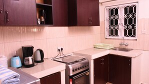 Una cocina funcional con estufa, horno y cafetera. Hay armarios sobre la encimera y una ventana con celosías decorativas.