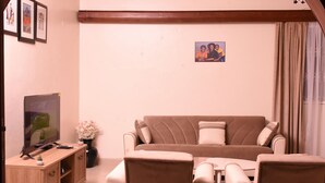 Una sala de estar con un sofá color crema, un aparador de madera, un televisor y una mesita.