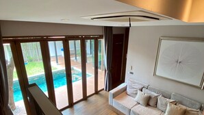 A modern living room with a sofa, a round table, and a view of a swimming pool through large glass doors. -  Serava Pet-Friendly Pool Villa Huahin (Hua Hin)