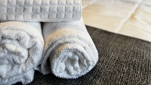 En pænt redt seng med et gråt og hvidt dynebetræk, en grå sengegavl og en mørkegrå, struktureret sofa.