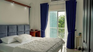 Ein Schlafzimmer mit Bett, Nachttisch, einem Fenster mit Vorhängen und Blick ins Grüne.