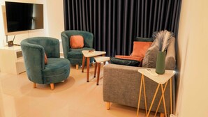 Ein modernes Wohnzimmer mit türkisfarbenen Sessel, einem grauen Sofa und einem flachbildfernseher an der Wand.