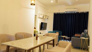 Ein modernes Wohnzimmer mit einem мраморном Esstisch, beigen Sesseln, einem blauen Sofa und einem an der Wand befestigten Flachbildfernseher.