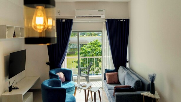Ein modernes Wohnzimmer mit einem Flachbildfernseher, einem Sofa, einem Couchtisch und einem Balkon mit Blick auf Grünflächen.