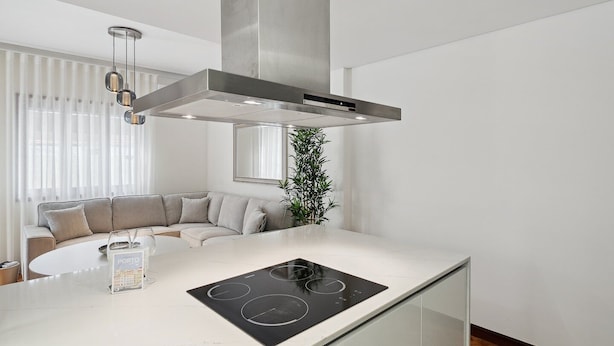 A modern kitchen with a white countertop, a built-in stove, and a stainless steel range hood.