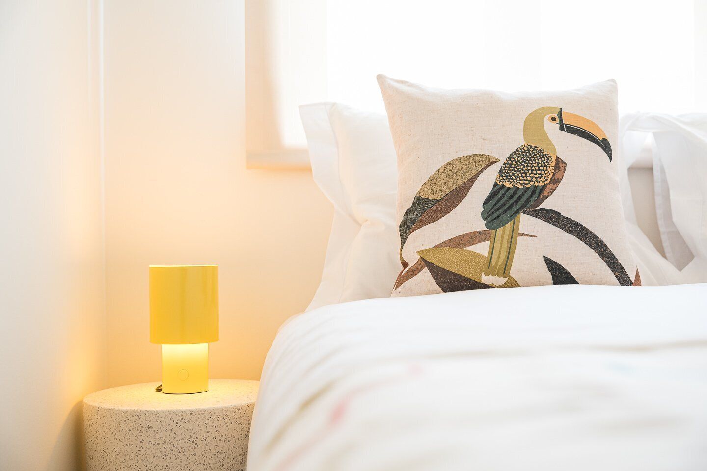 Ein Bett mit weißer Bettwäsche und einem Kopfkissen mit Vogelmotiv.