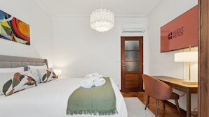 A hotel room with a bed, a desk, a chair, a TV, and a painting on the wall.