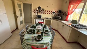 A compact kitchen with a dining table set for four, equipped with basic appliances and a window with red curtains. - A pleasant ground floor 5 minutes' walk from the beach (Hergla)