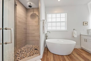 Un baño moderno con una bañera independiente, cabina de ducha con paredes de vidrio y una ventana con persianas.